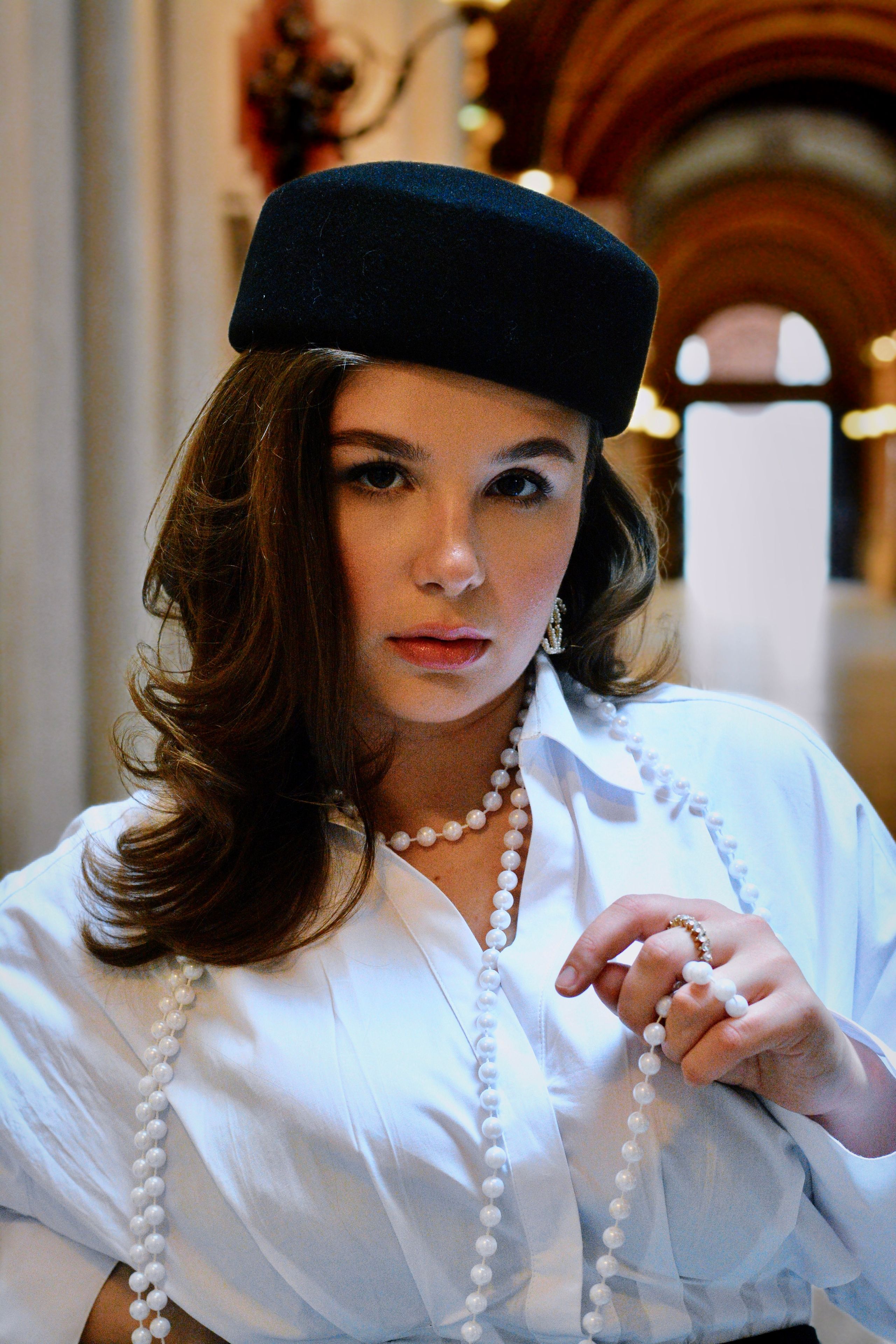 A striking portrait of a young woman wearing a black beret and pearl necklaces in an opulent Viennese interior.