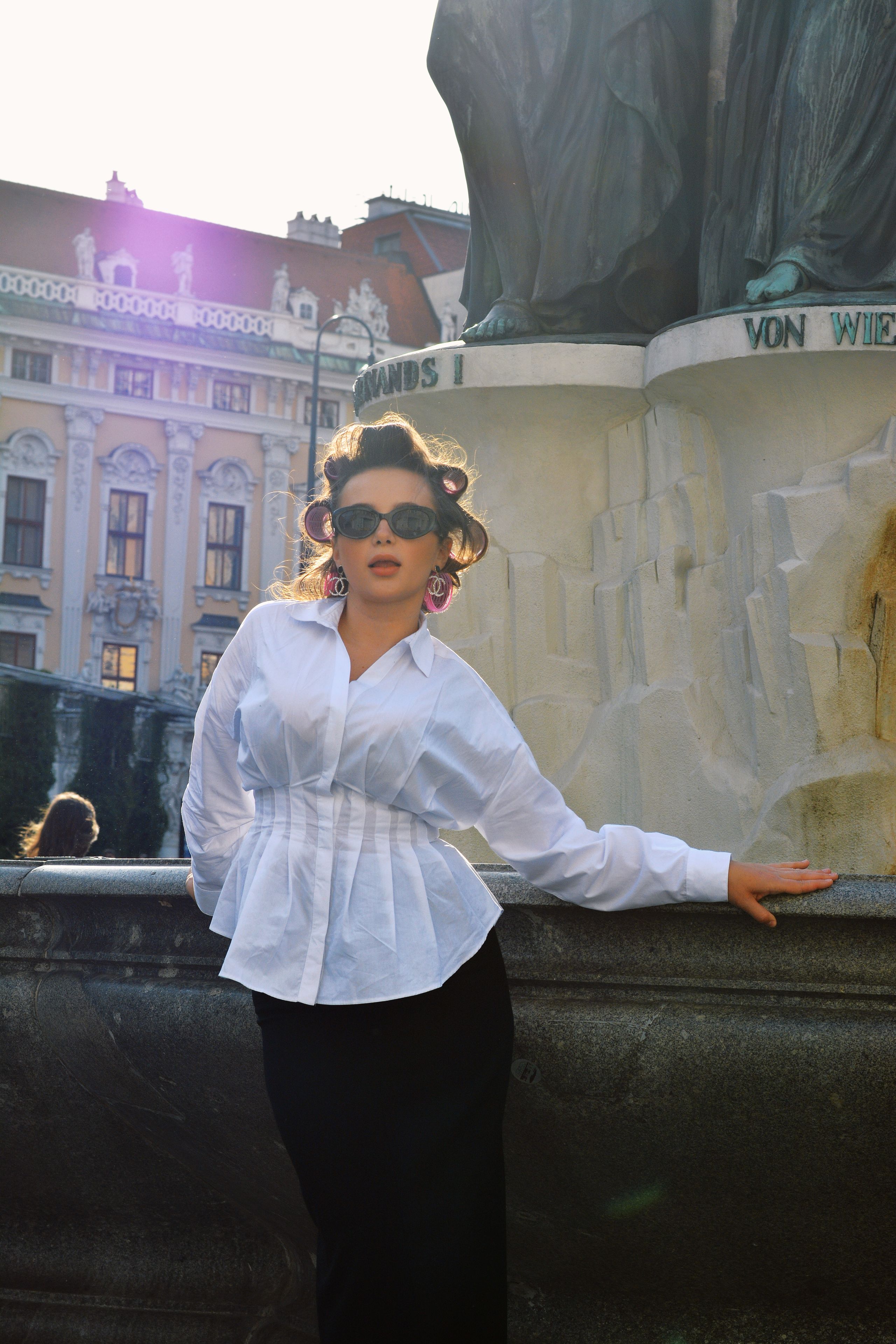 A stylish woman in a white blouse and black skirt poses near a monumental statue in Vienna, capturing a sophisticated portrait.