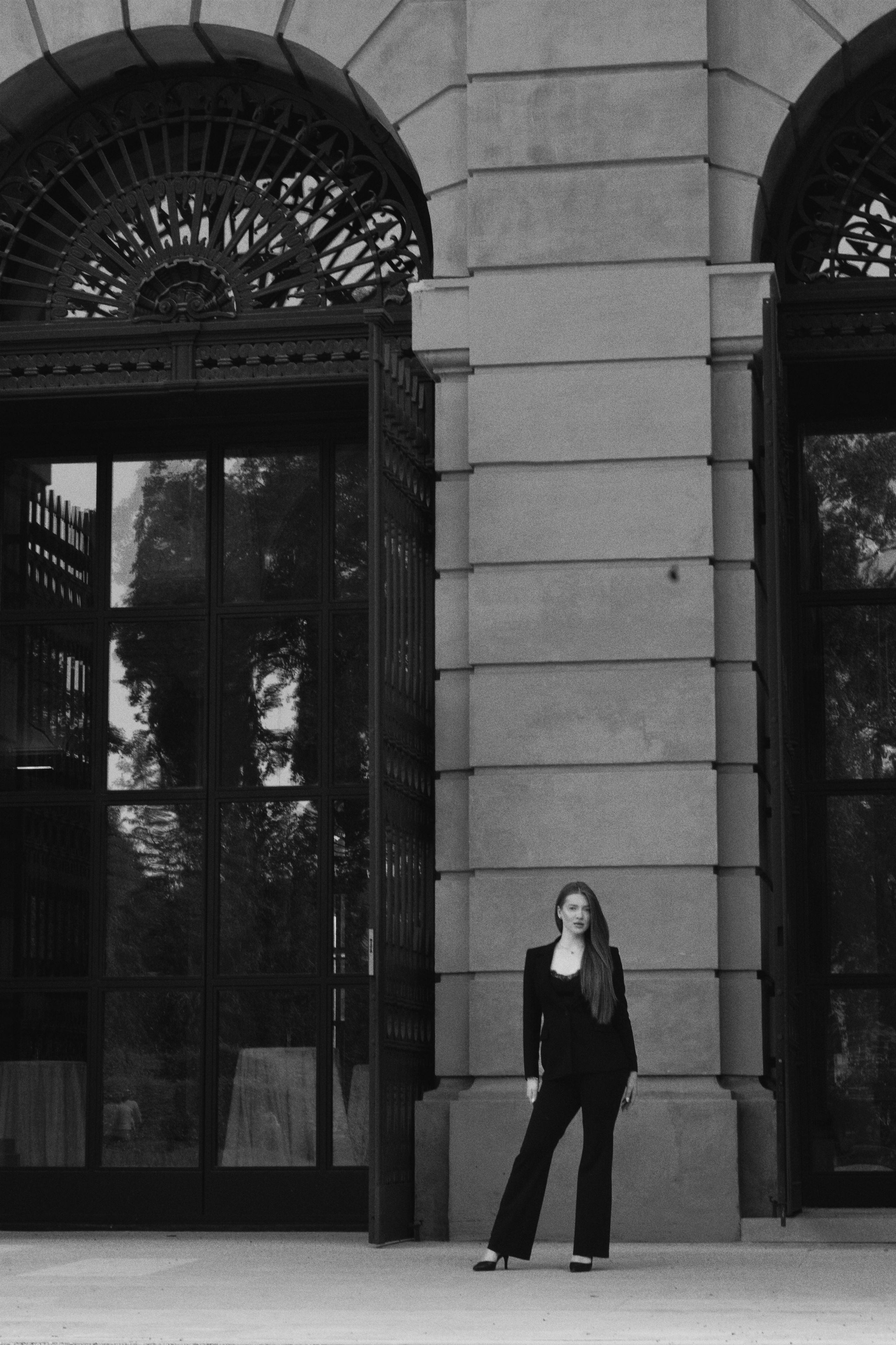 A striking black and white portrait of a woman standing against the grand, neoclassical facade of a Viennese building.